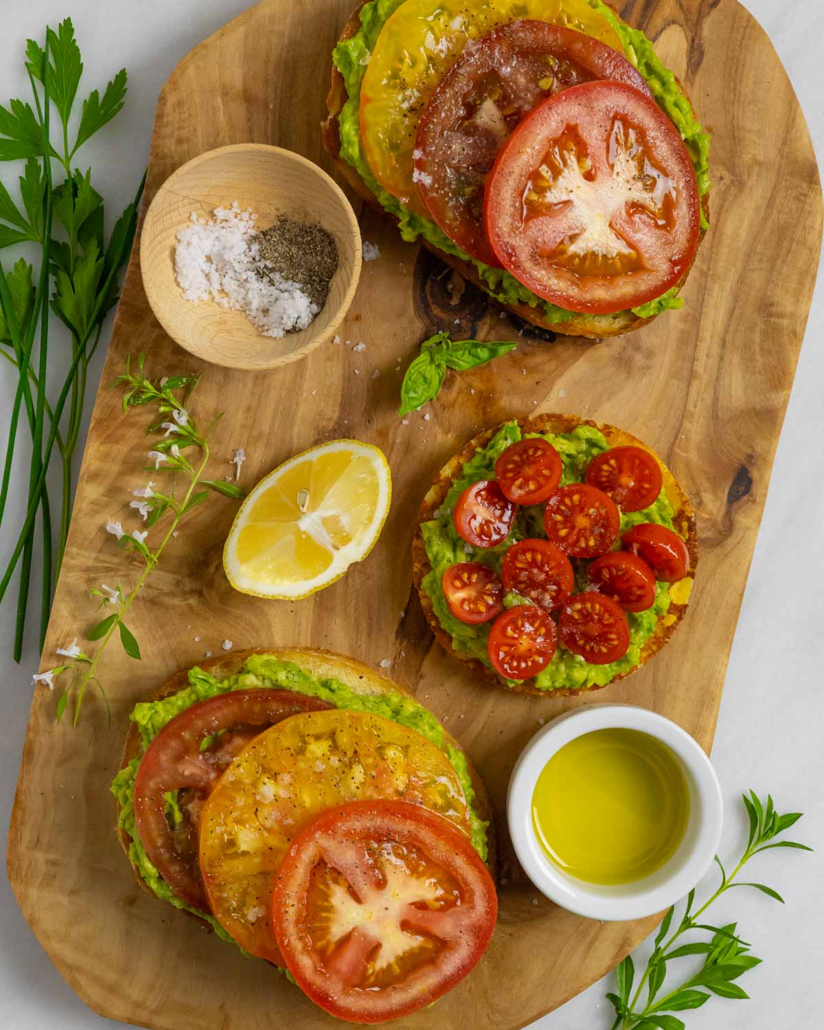 Wood board with slices of keto avocado toast with spices, ramekin of olive oil, and herbs as garnish.