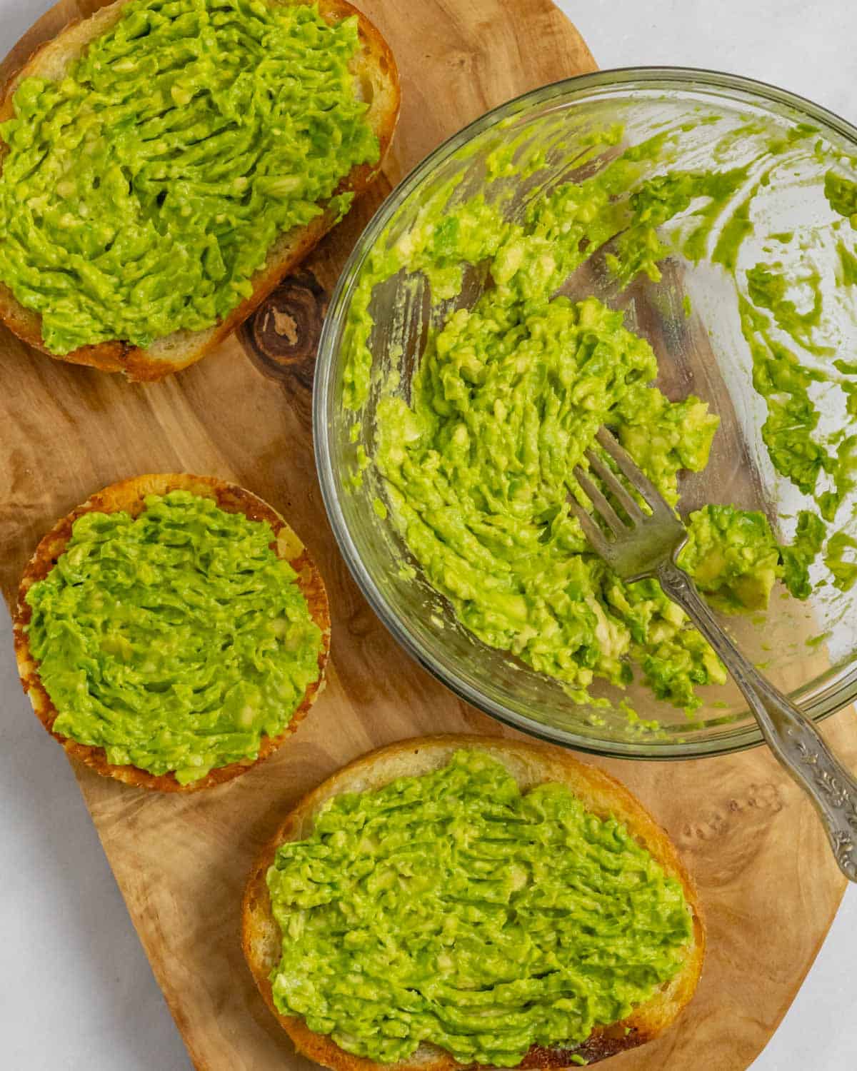 Mashed avocado in a bowl, and spread on three slices of toast.