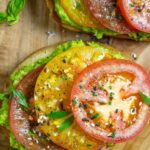 Low carb avocado toast with slices of red and yellow tomatoes sprinkled with seasonings and fresh herbs for garnish.