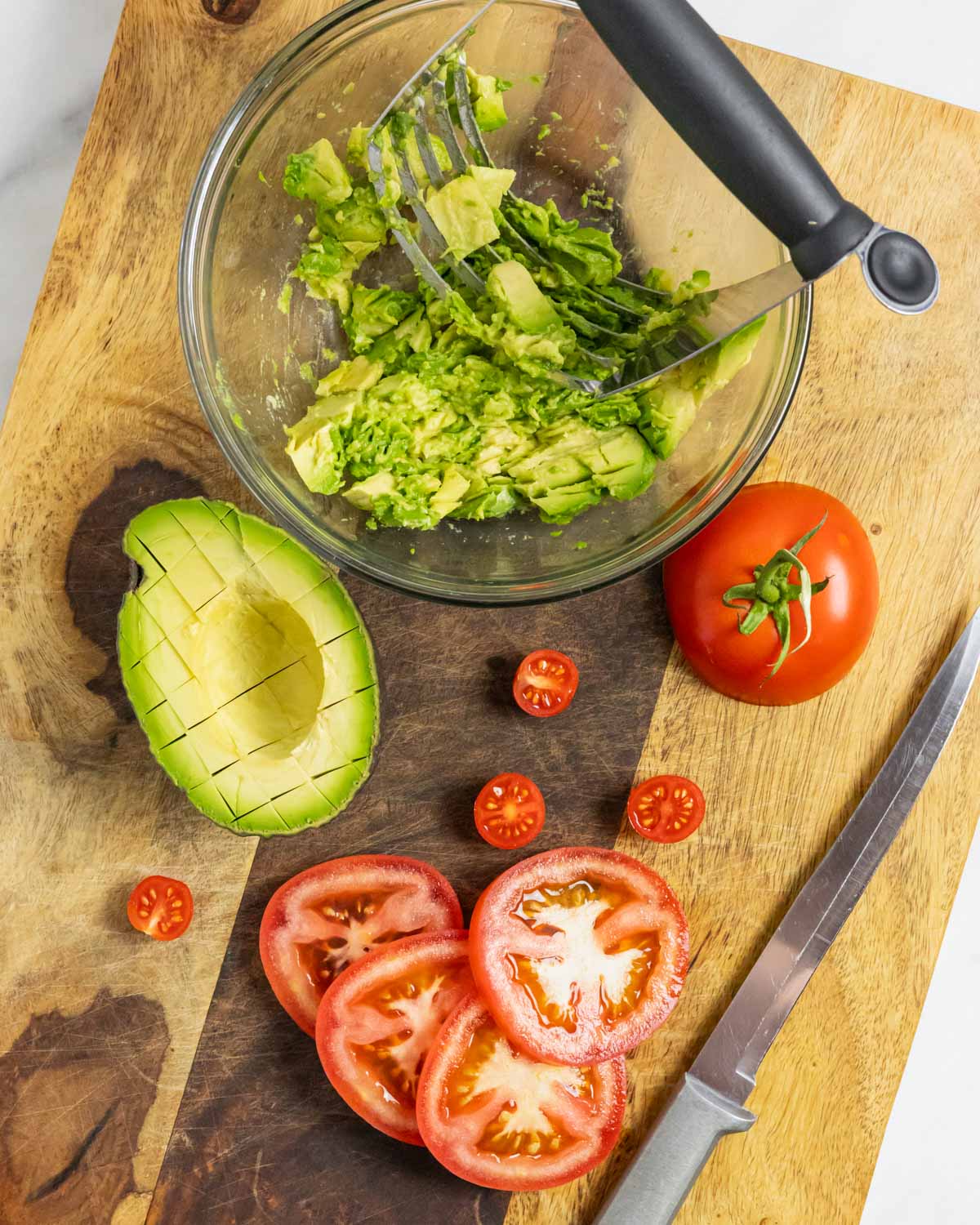 Sliced tomatoes, avocado and mashed avocado in a bowl on a board.