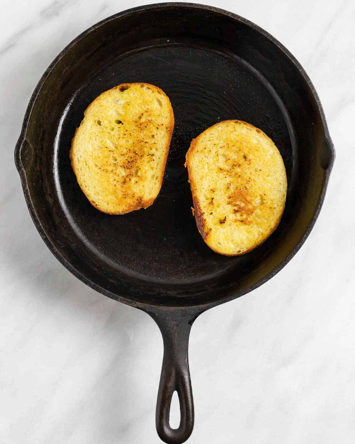 Cast iron fry pan with two slices of buttered and toasted bread.