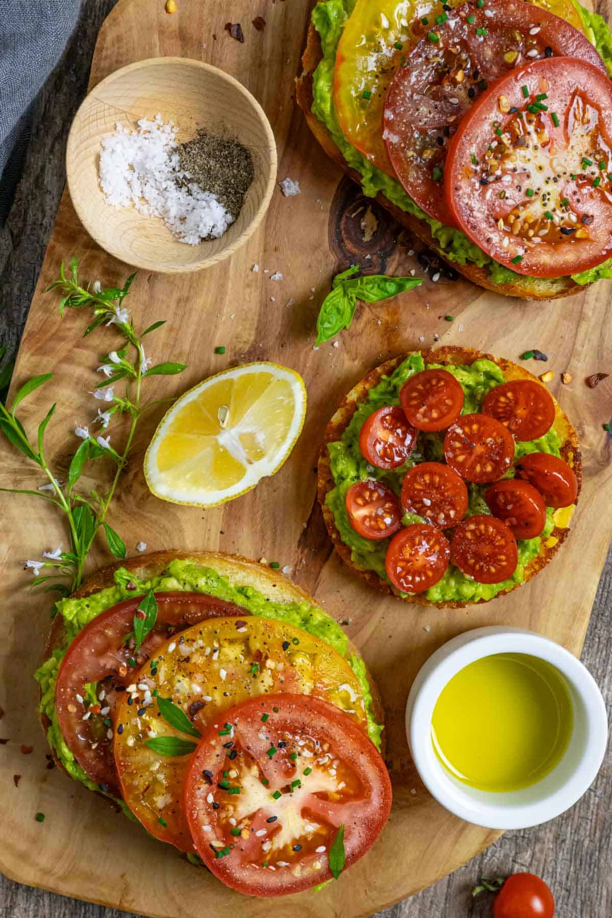 Avocado toast with tomatoes on three different breads on a board with olive oil, lemon wedge and seasonings.