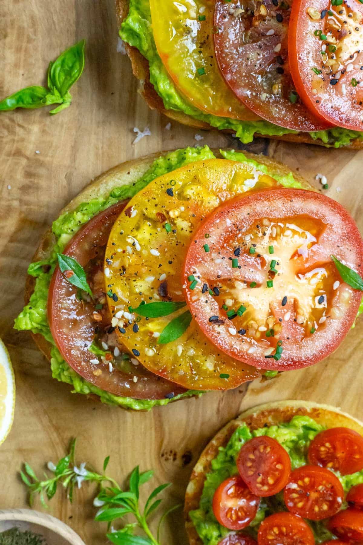 Low carb avocado toast with slices of red and yellow tomatoes sprinkled with seasonings and fresh herbs for garnish.