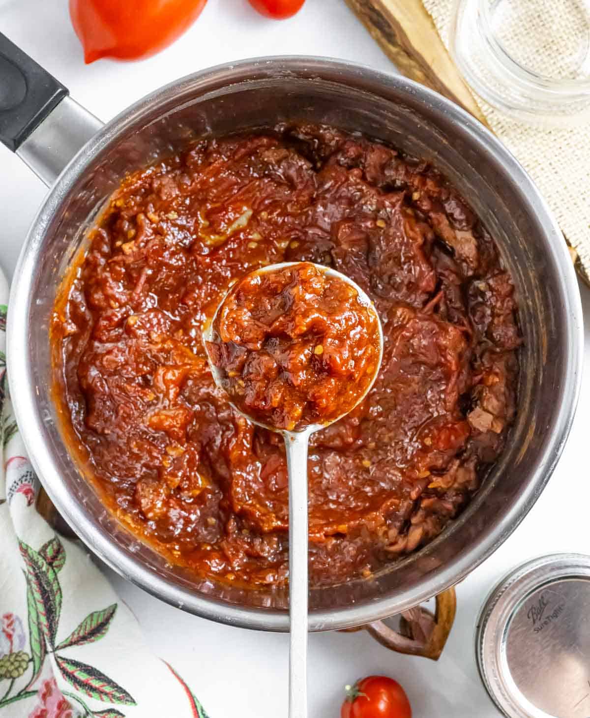 Cooked down tomato jam in a sauce pan with a spoonful positioned over the pan.