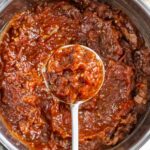 Cooked down tomato jam in a sauce pan with a spoonful positioned over the pan.