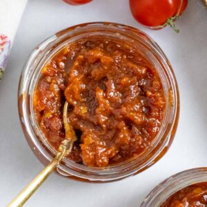 Tomato jam in a jar with a golden spoon in it.