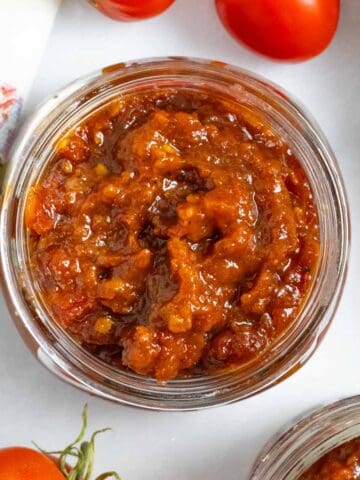 Jar of tomato marmalade jam on a marble board.