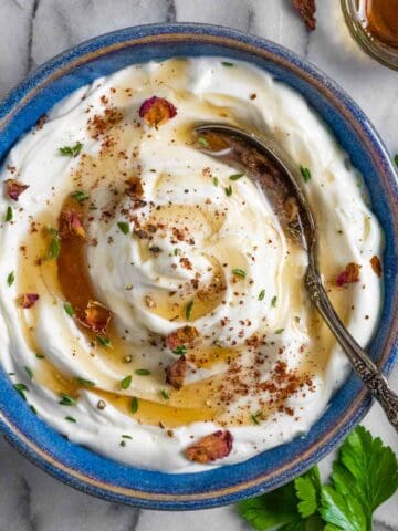 Ricotta party dip in a blue bowl with a spoon topped with maple syrup and herbs.