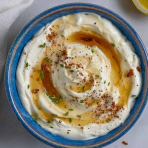 Ricotta party dip in a blue bowl topped with maple syrup and herbs.