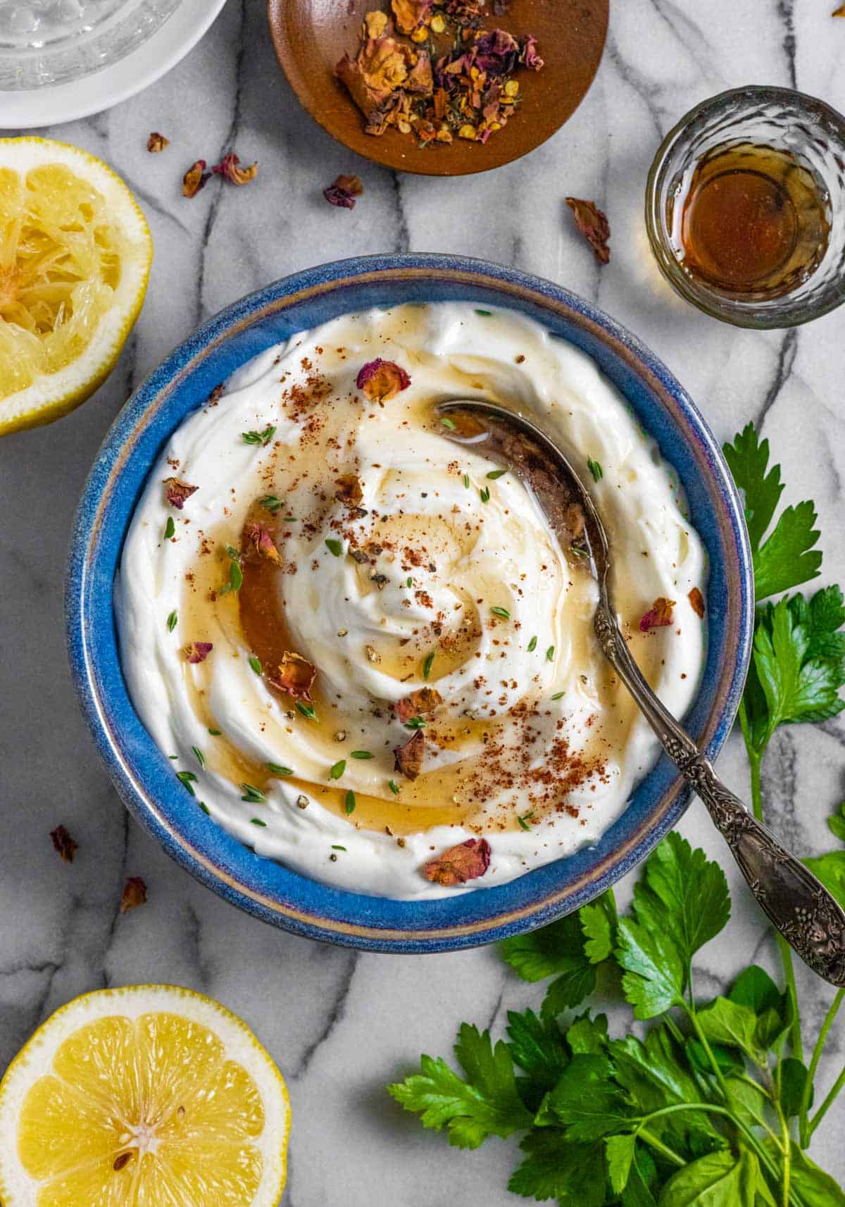 Whipped ricotta party dip sprinkled with herbs and maple syrup in a blue ceramic bowl with a spoon.