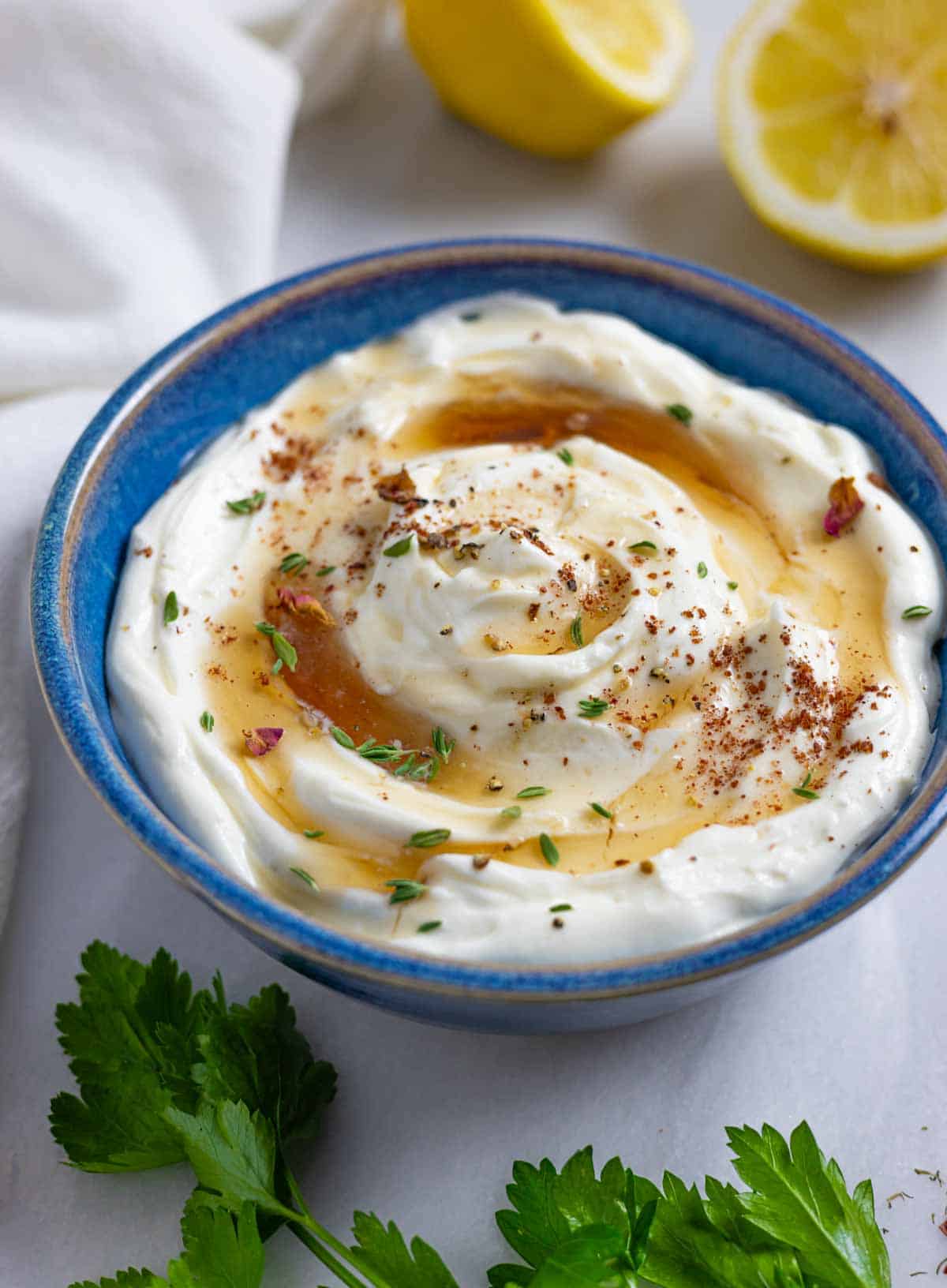 Whipped ricotta dip in a blue ceramic bowl topped with herbs and drizzled with sugar-free maple syrup.