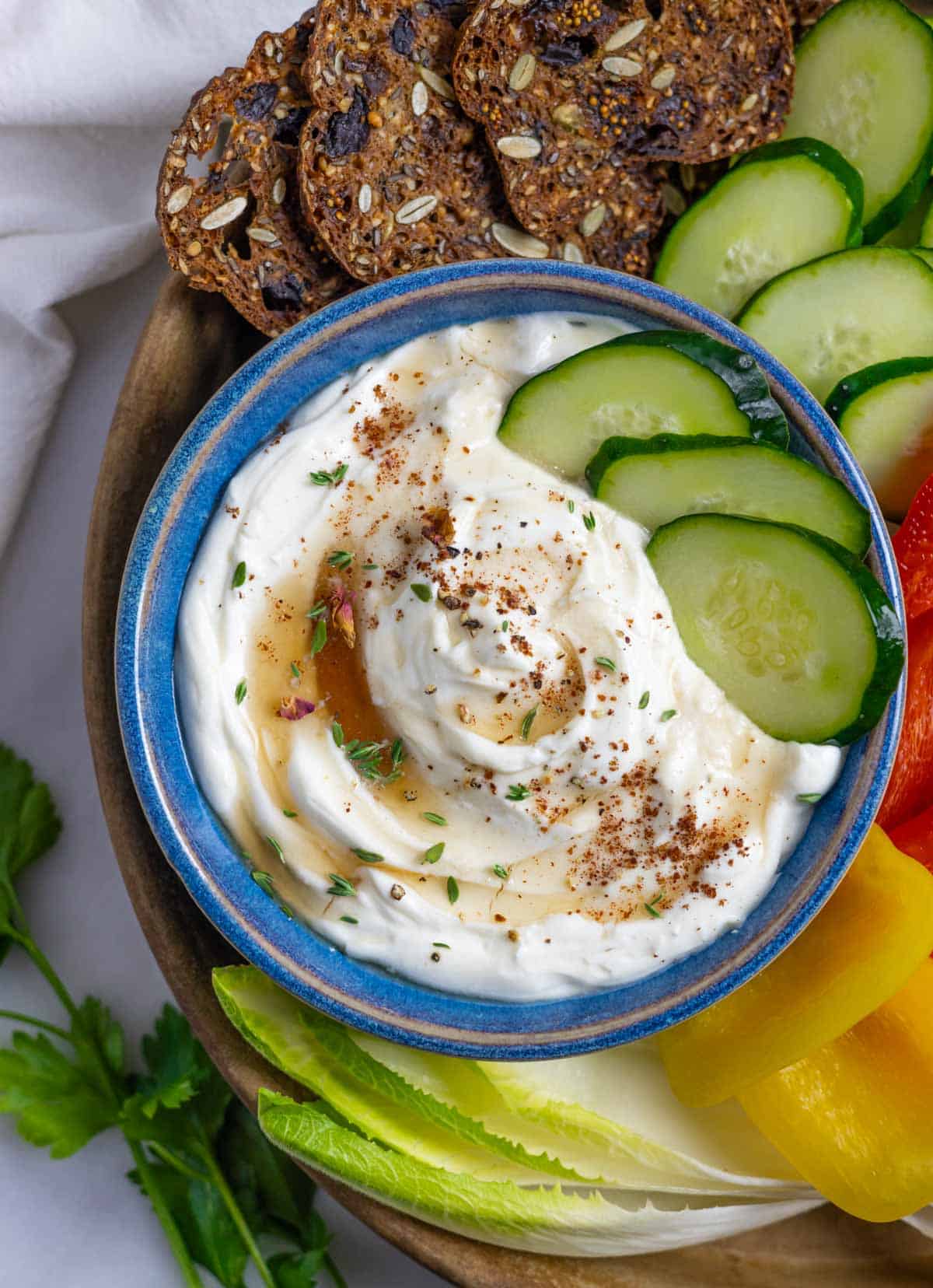 Blue bowl of ricotta keto appetizer dip with cucumber slices in the bowl and next to it on a tray with crackers.