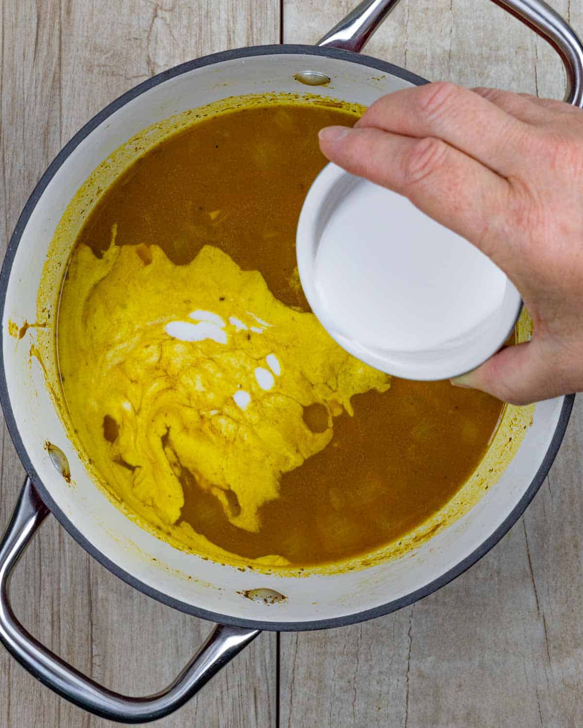 Ramekin of coconut milk being poured into carrot pumpkin soup.