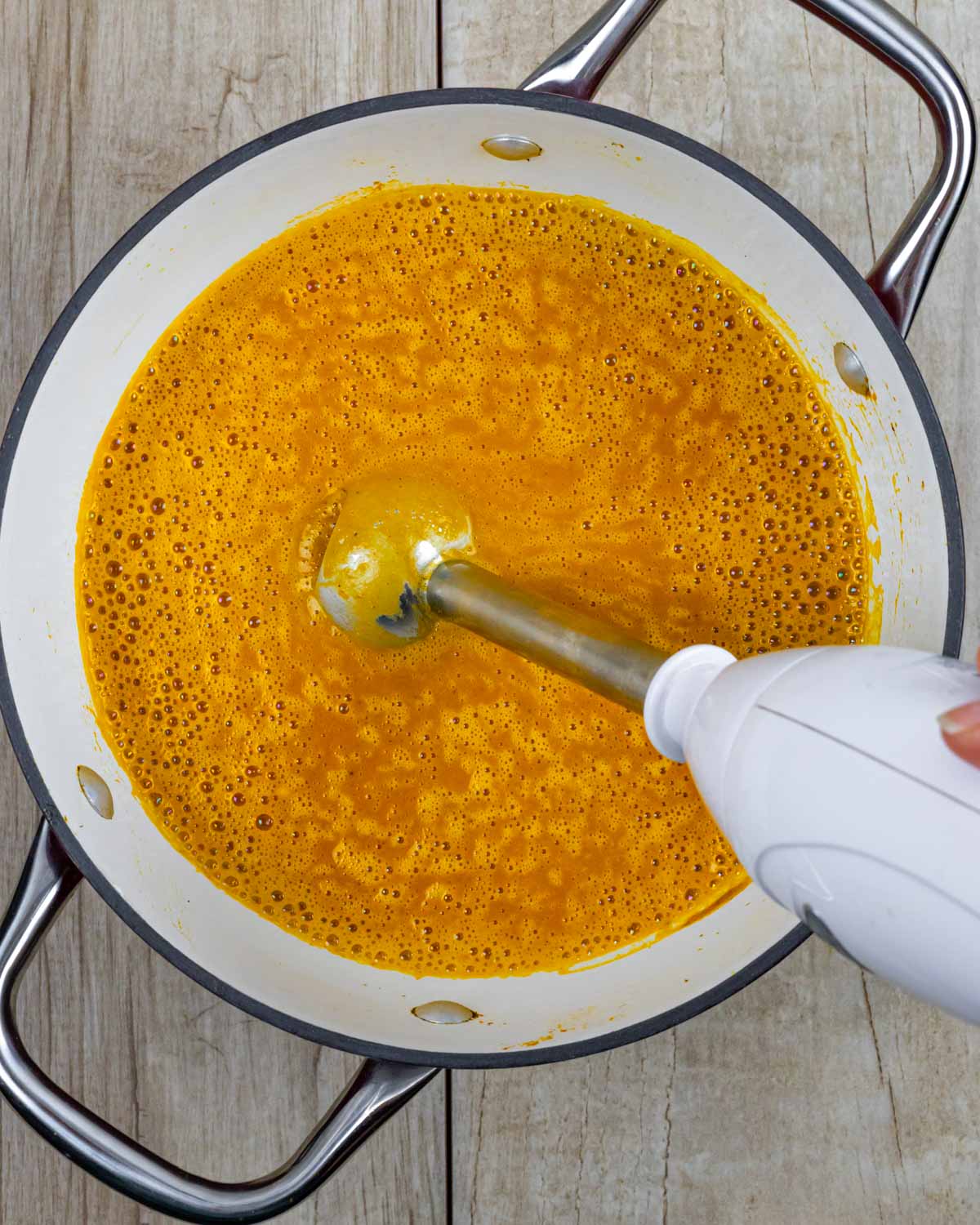 Immersion blender in a pot of pumpkin and carrot soup blending the cooked ingredients together.