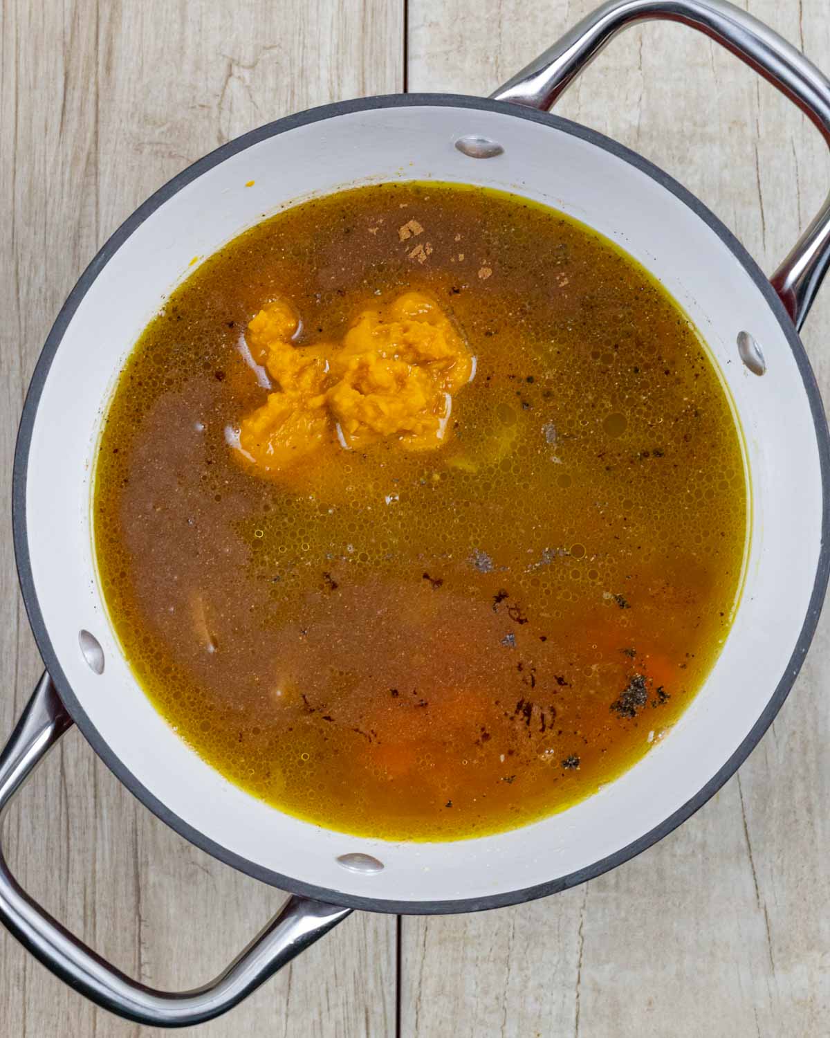 Broth, pumpkin, carrots and spices added to soup pot ready to stir and simmer.