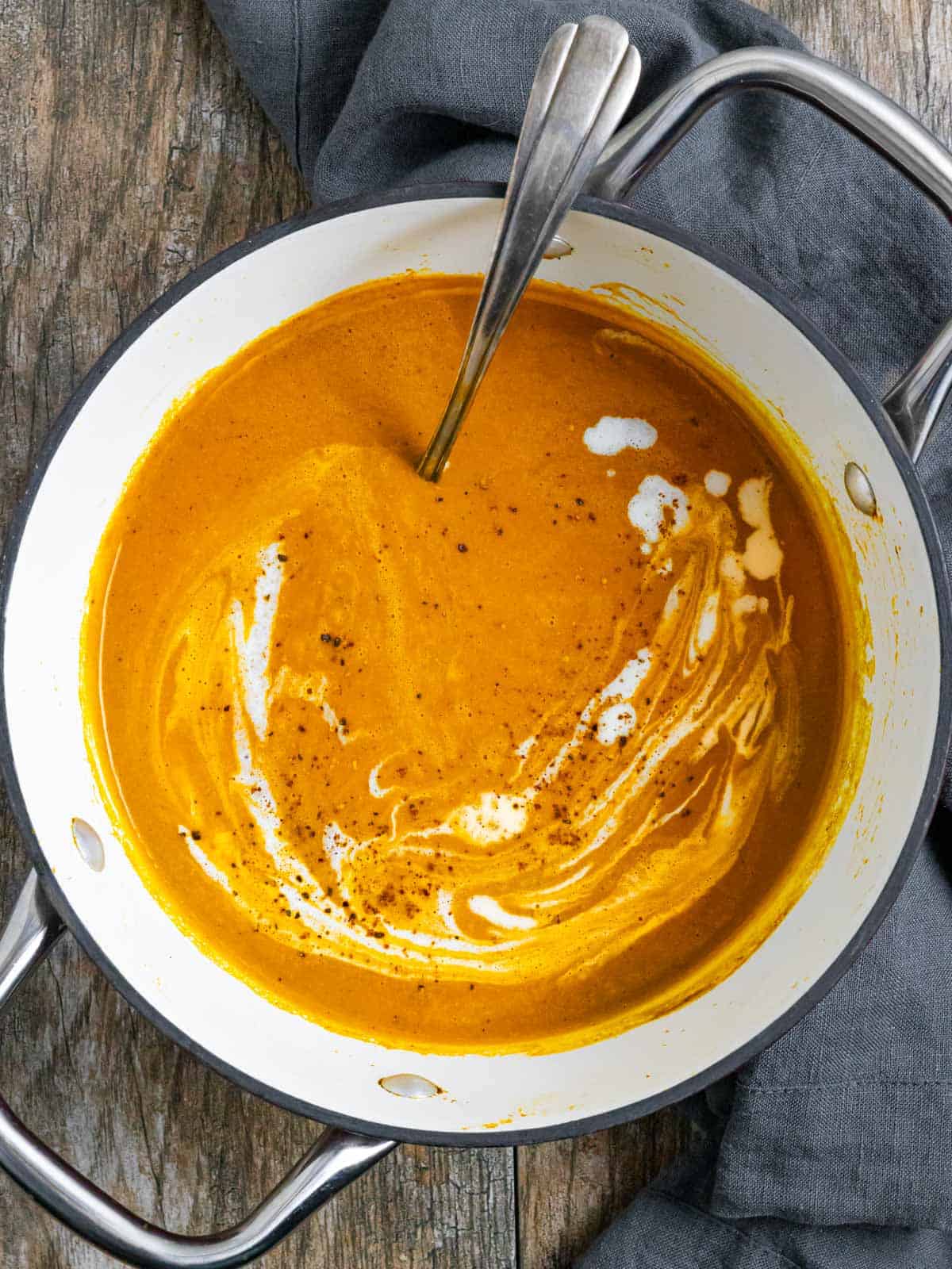 Pot of pumpkin soup with carrot with coconut milk and spices on top and a spoon in the pot.