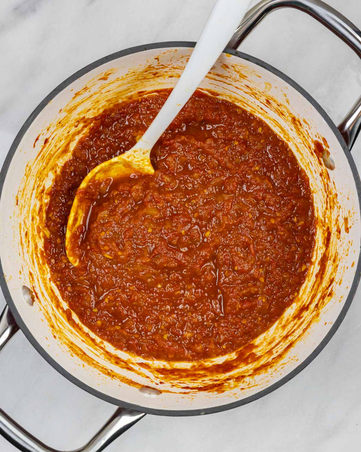 Tomato onion chutney ingredients simmered in medium saucepan with a large spoon.