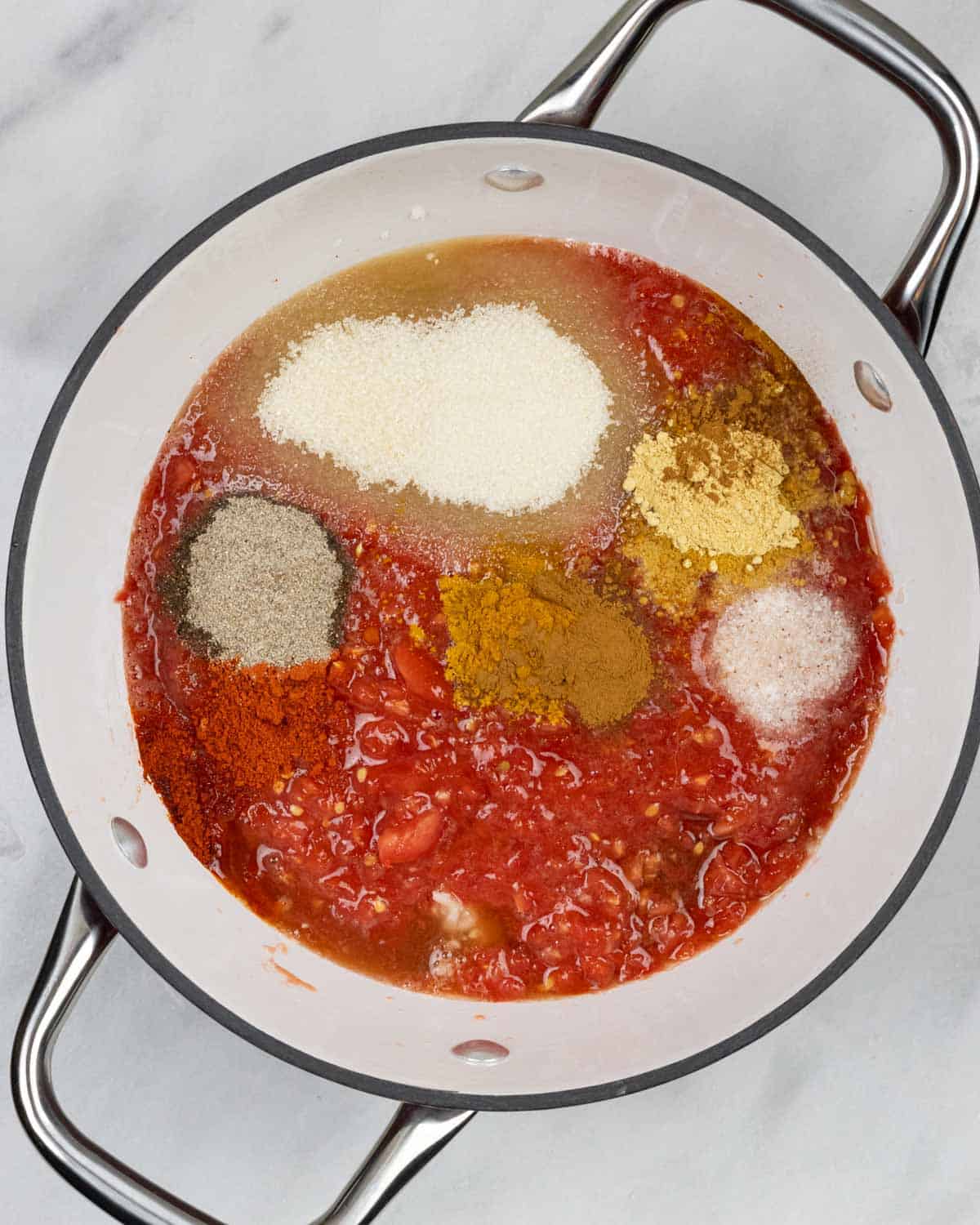 Processed tomatoes, ingredients and spices in saucepan ready to mix together.