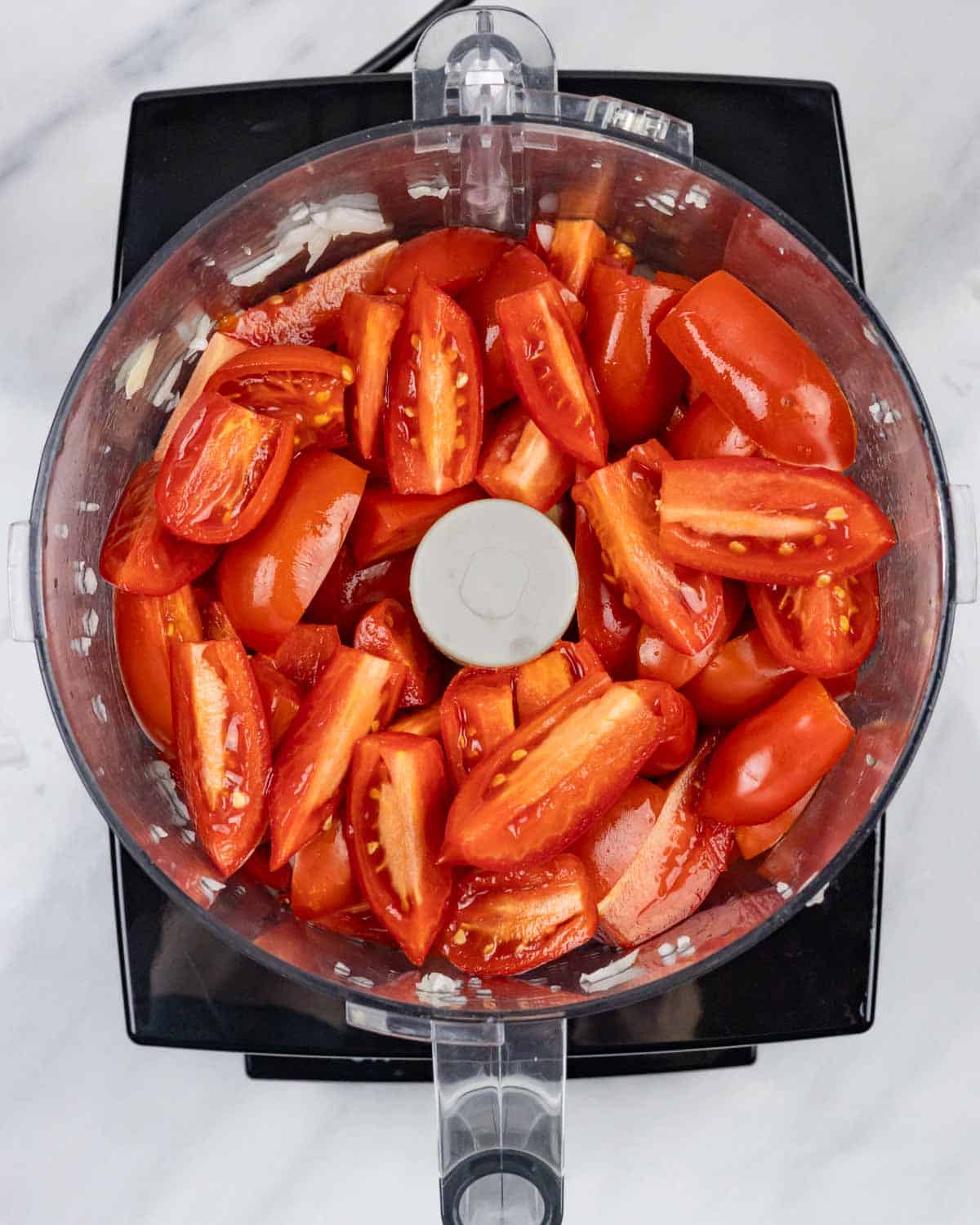 Tomatoes in wedges in a food processor bowl ready to process.