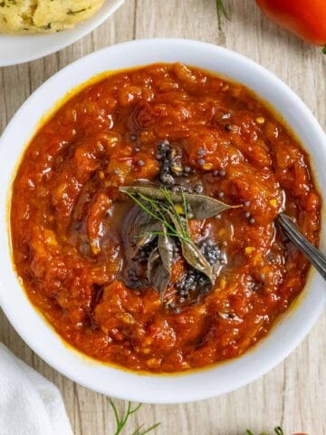 White bowl of tomato onion chutney with herbs on top and a spoon in the bowl.