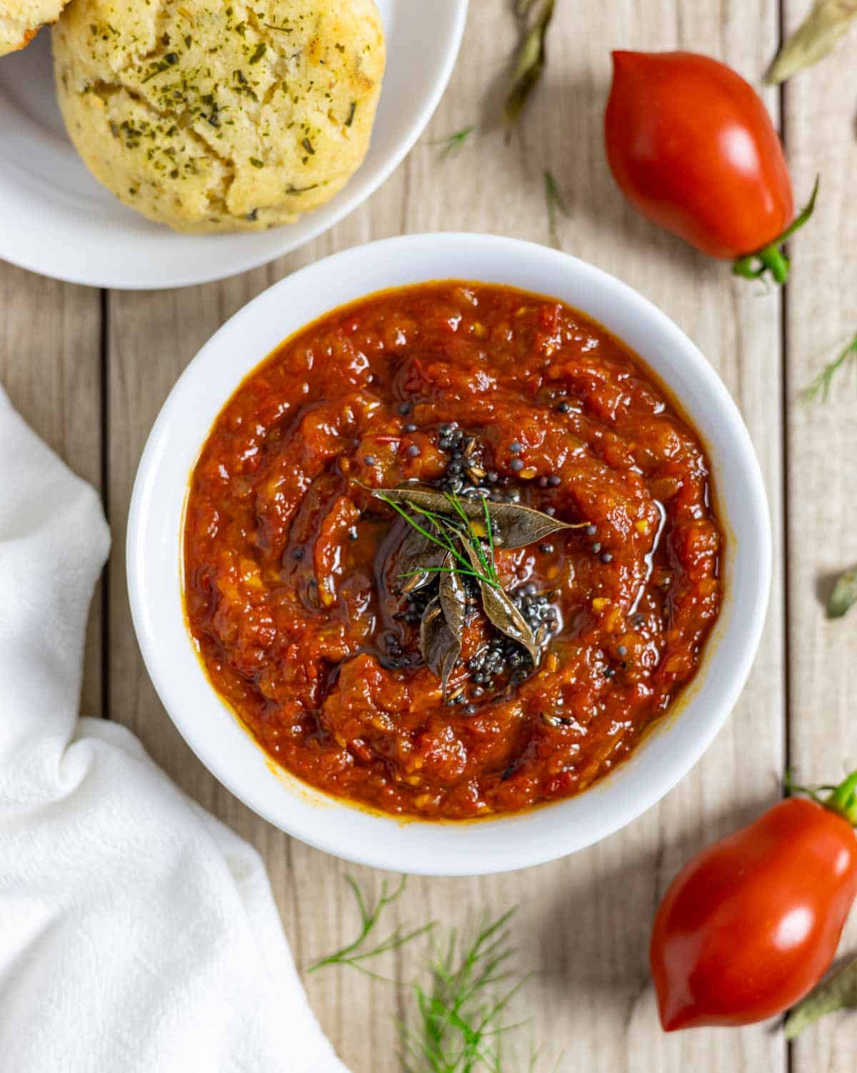 Bowl of tomato and onion chutney topped with herbs, next to a plate of chedar biscuits.