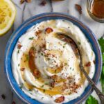 Whipped ricotta party dip sprinkled with herbs and maple syrup in a blue ceramic bowl with a spoon.