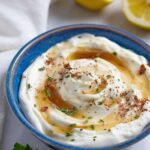 Whipped ricotta dip in a blue ceramic bowl topped with herbs and drizzled with sugar-free maple syrup.