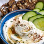 Blue bowl of ricotta keto appetizer dip with cucumber slices in the bowl and next to it on a tray with crackers.