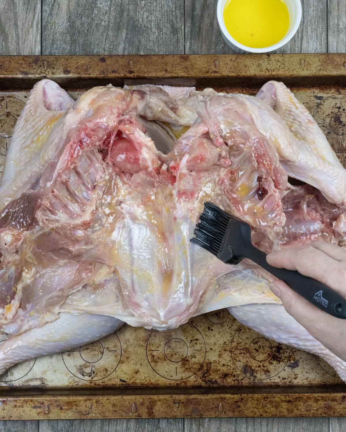 Butterflied raw turkey cavity being buttered with a basting brush.