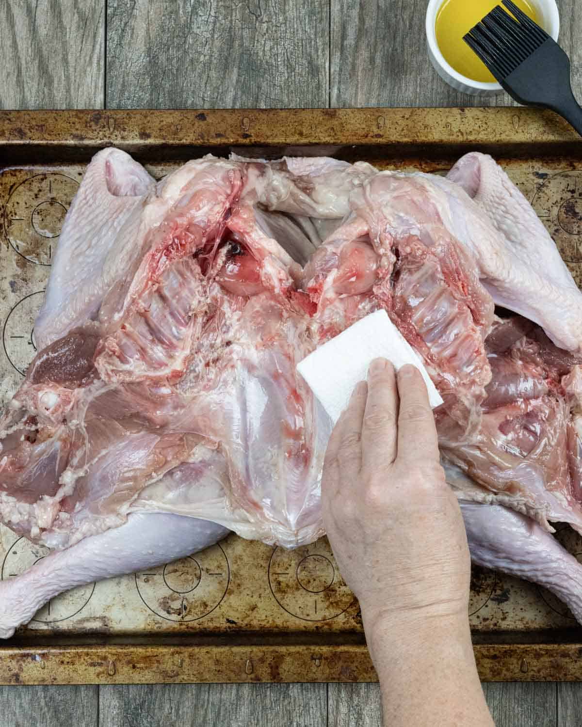 Butterflied raw turkey, breast down on a tray with inside being pat dry with a paper towel.