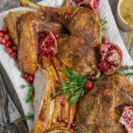 Smoked turkey breast slices, wings, leg quarters on a serving tray with herbs, cranberries and pomegranate halves.