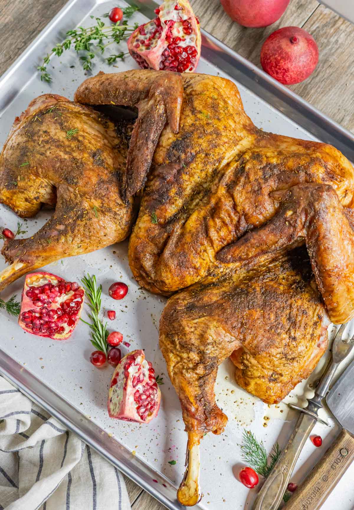 Golden smoked spatchcock turkey on a tray with fresh herb sprigs whole cranberries and pomegranate halves.