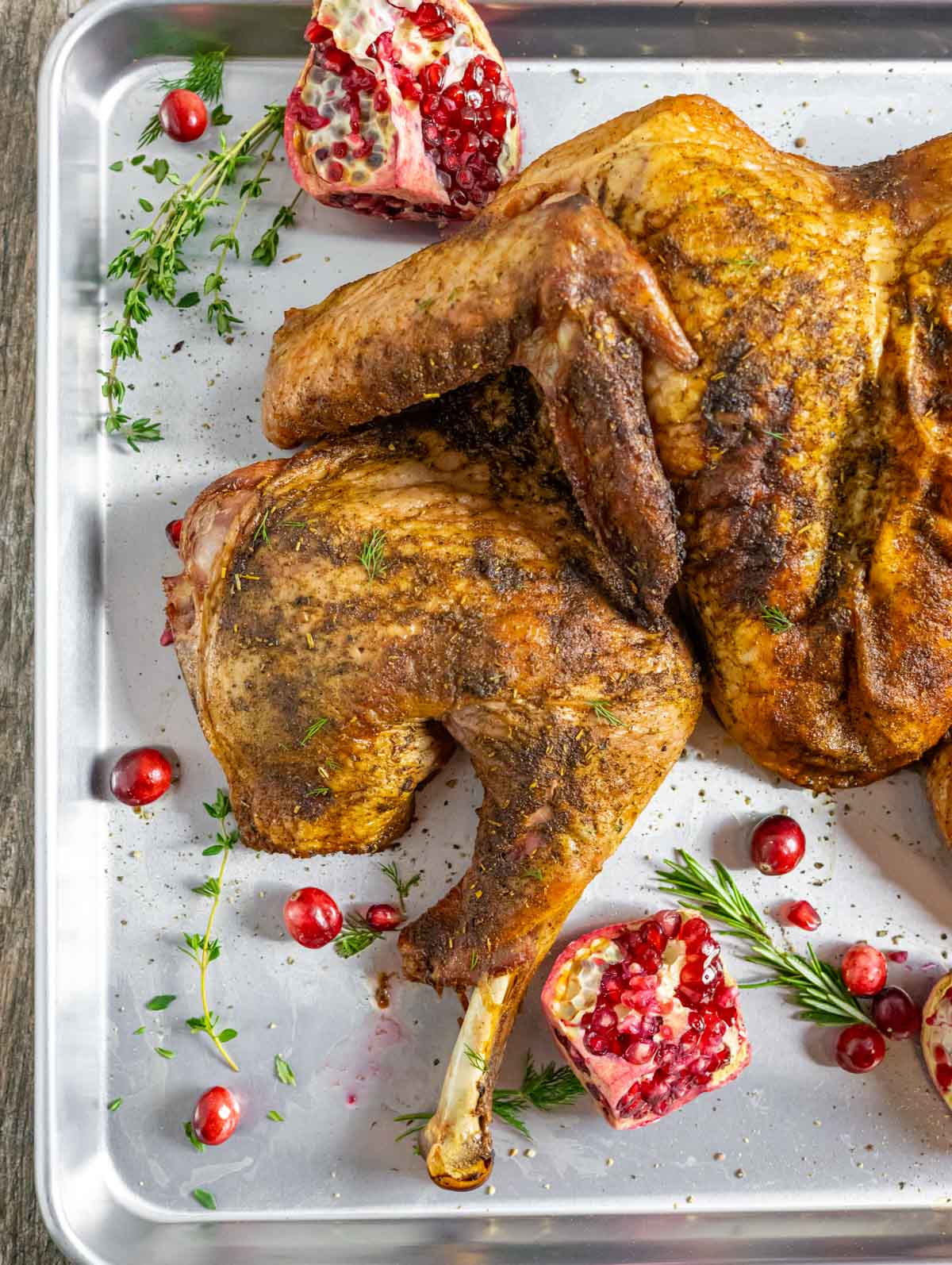 Smoked spatchcock whole turkey on a tray with pomegranate halves, cranberries and herbs.