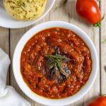 Bowl of tomato and onion chutney topped with herbs, next to a plate of chedar biscuits.