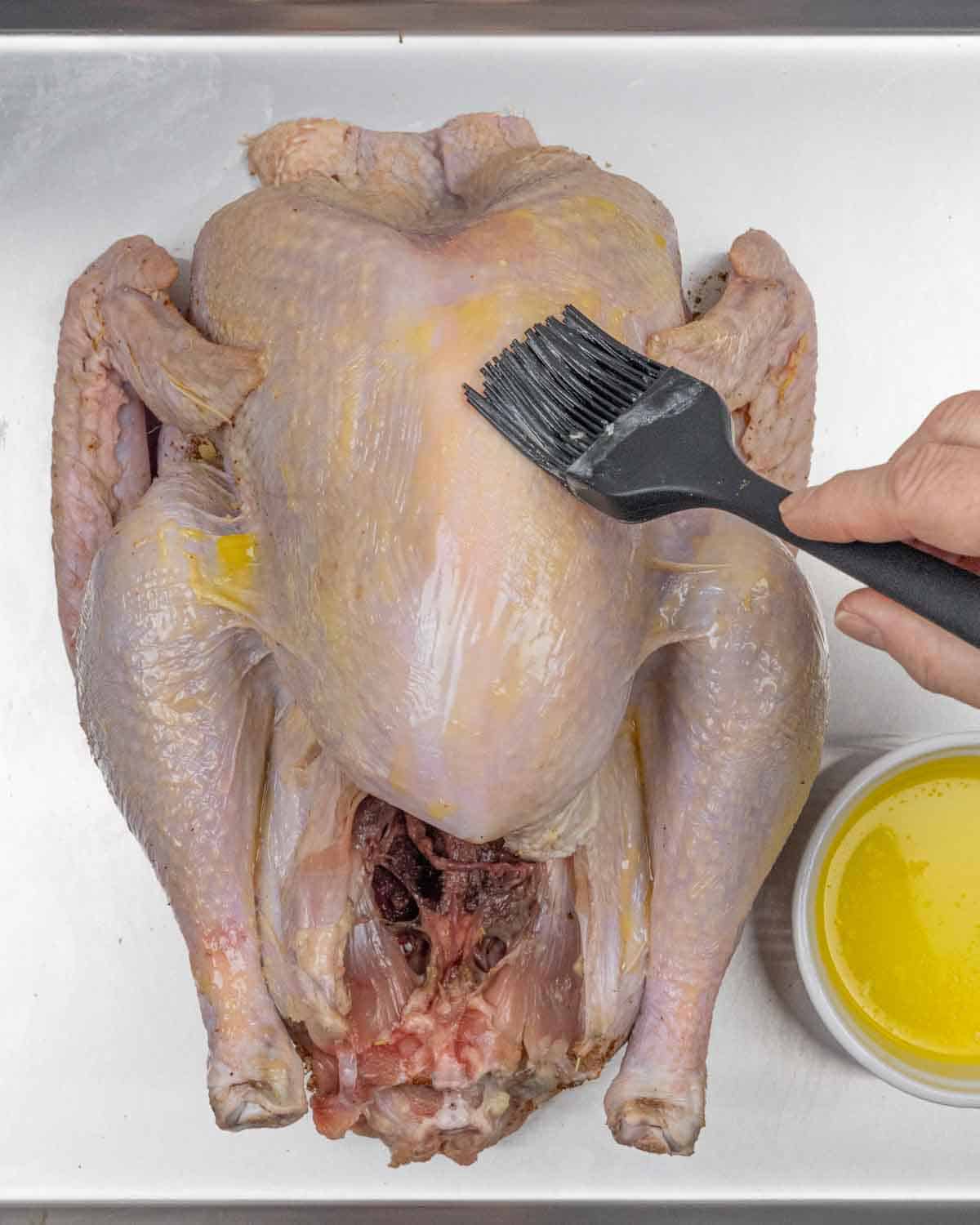 Raw whole turkey being brushed with butter from a ramekin of melted butter.