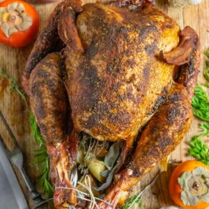 Traeger smoked turkey stuffed with aromatics on a board with herb sprigs and persimmons.