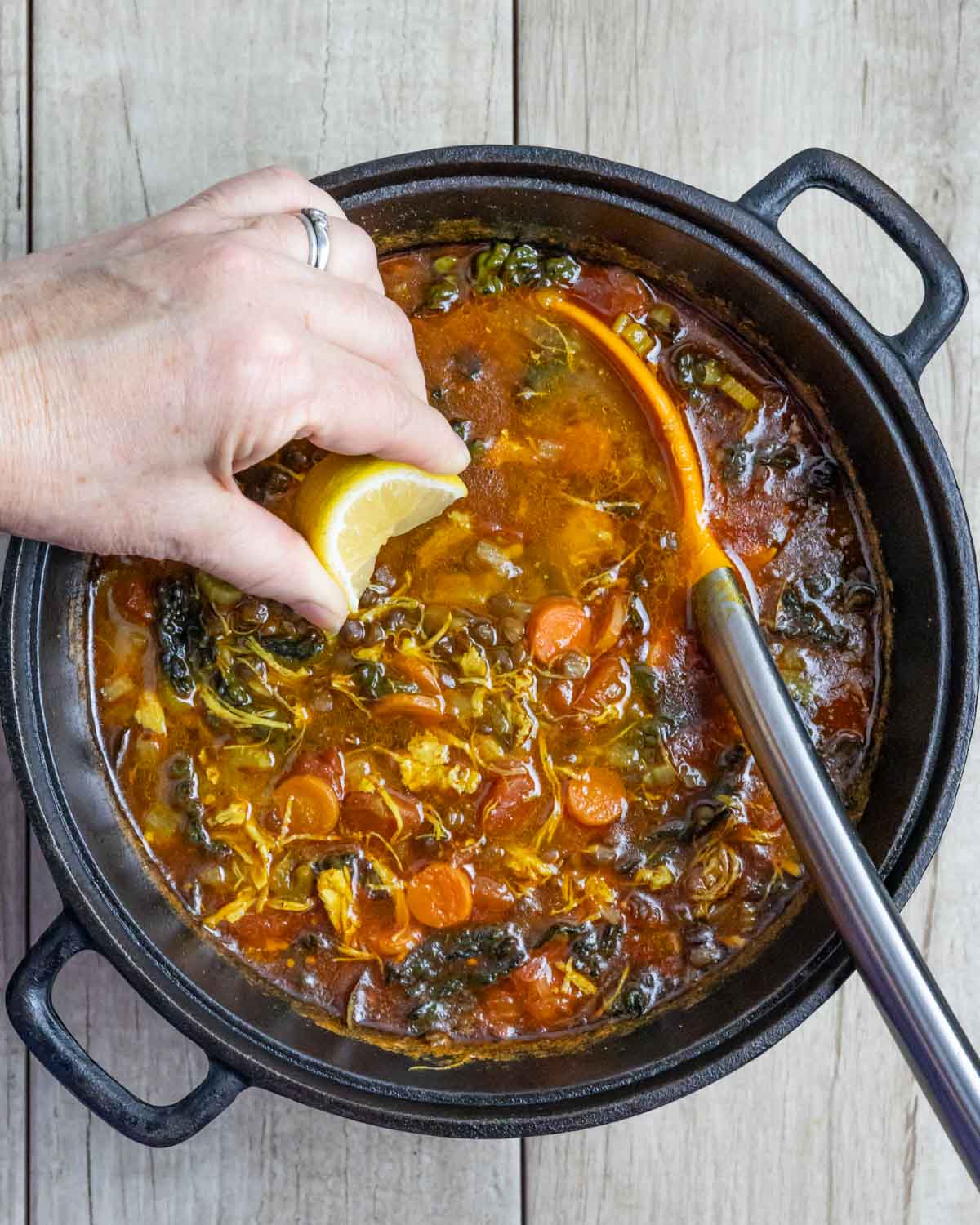 Pot of turkey lentil soup with serving spoon and a hand squeezing a lemon wedge into the soup.