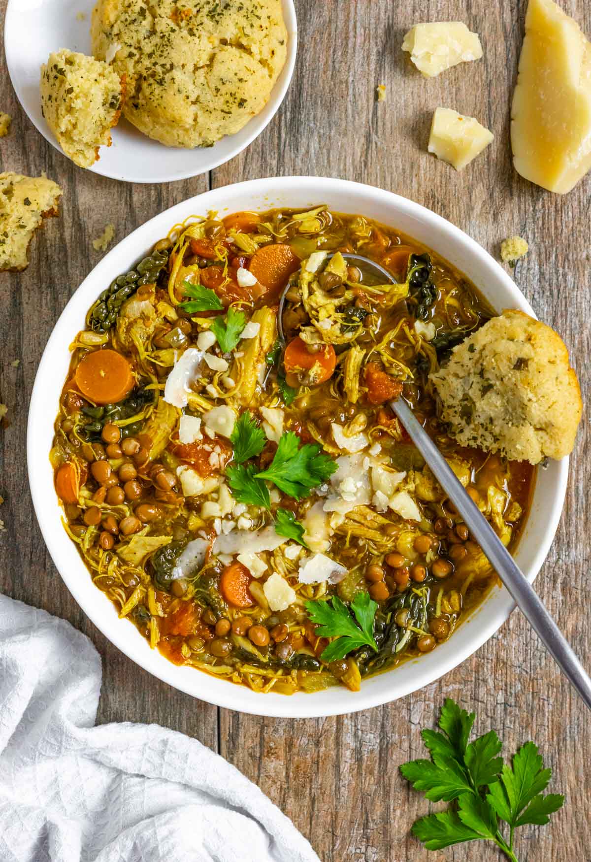 Keto turkey lentil soup in a white bowl with a spoon and part of a cheddar biscuit on a wood board.