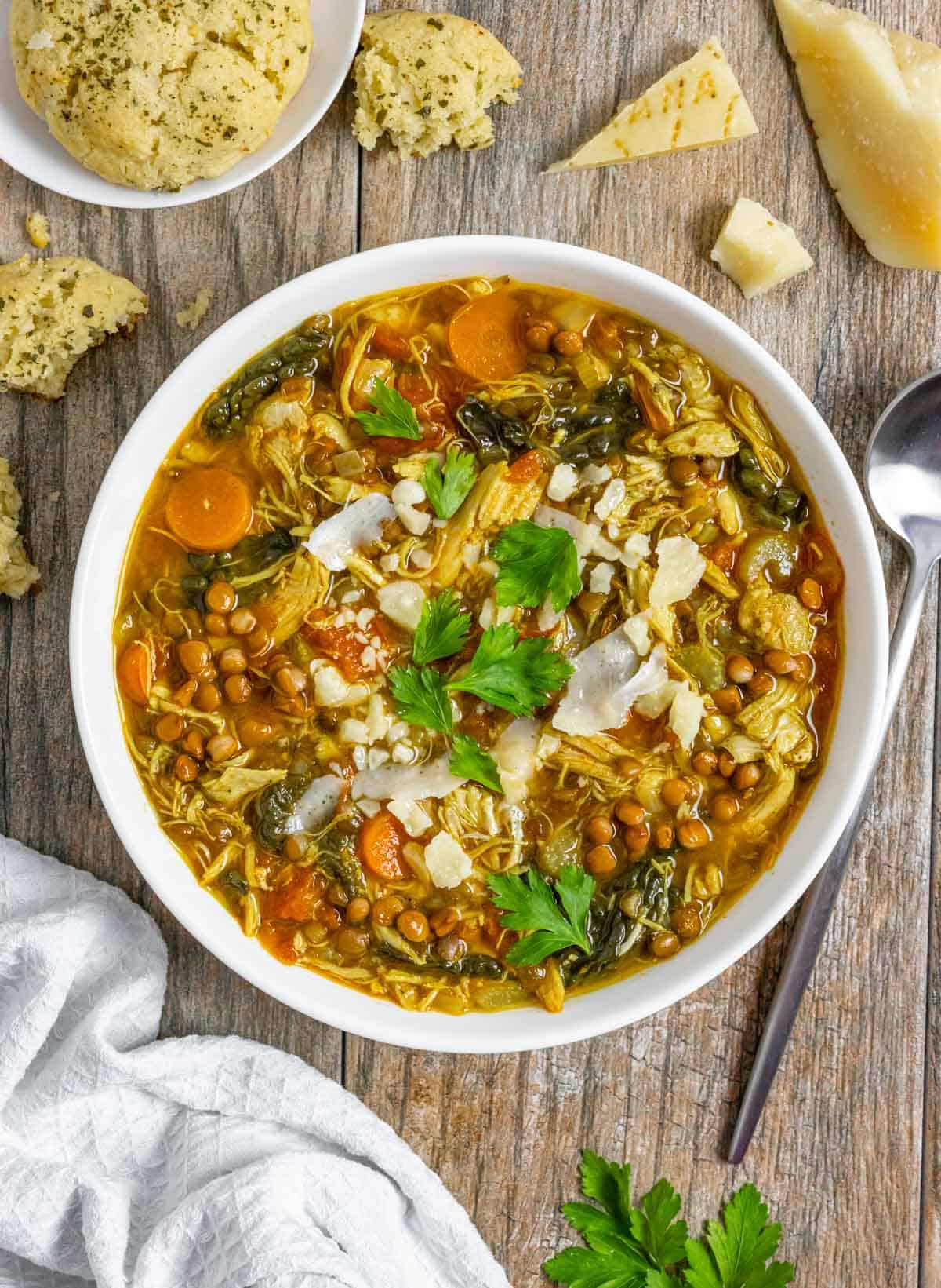 White bowl of turkey lentil soup topped with parsley and shaved parmesan on a wood board.