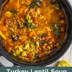 Turkey soup with lentils in a cast iron dutch oven with a serving spoon in the pot.