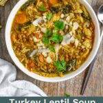 White bowl of turkey lentil soup topped with parsley and shaved parmesan on a wood board.