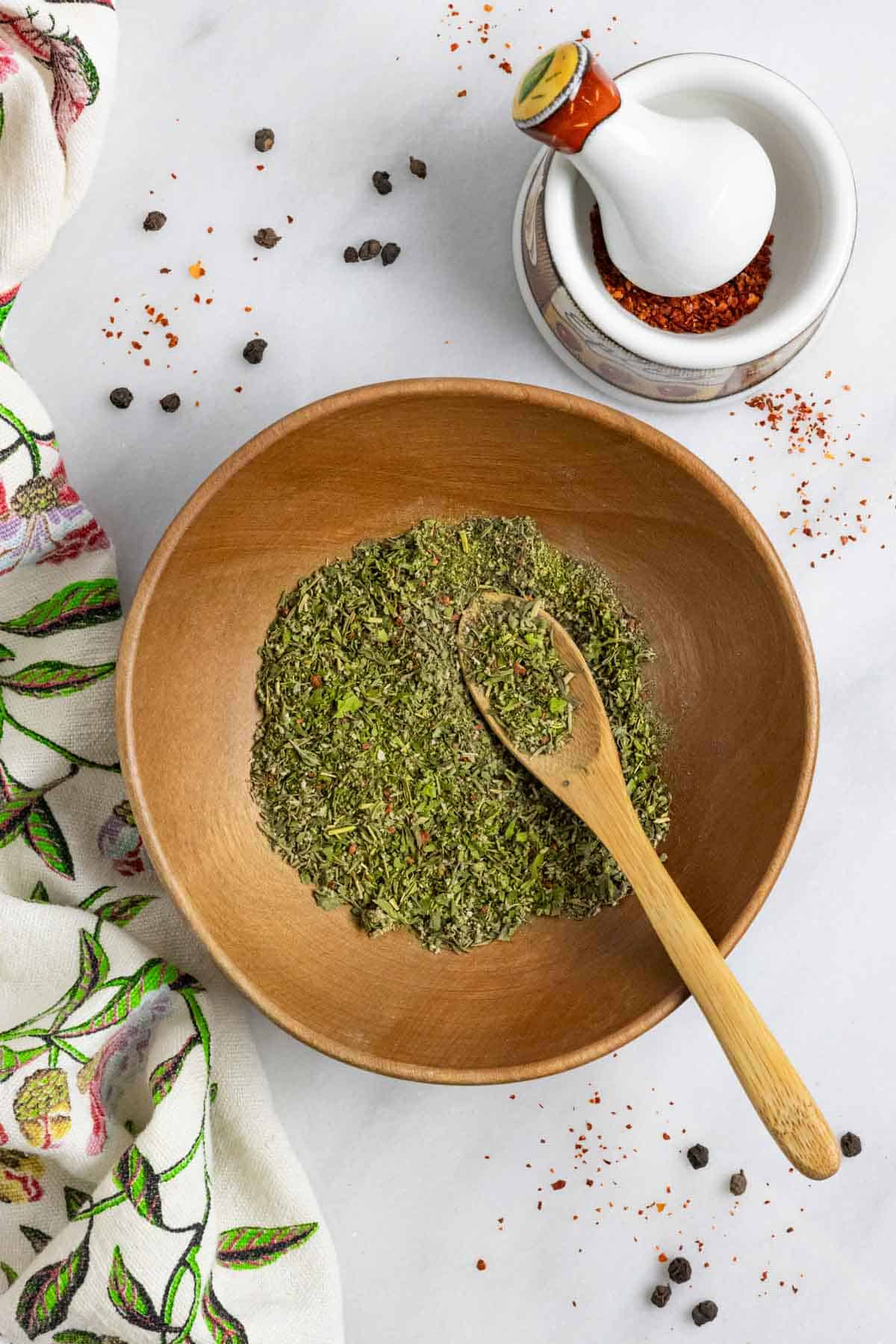 Wood bowl of mediterranean spice blend on a marble board with a small mortar and pestle.