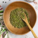 Wood bowl of mediterranean spice blend on a marble board with a small mortar and pestle.