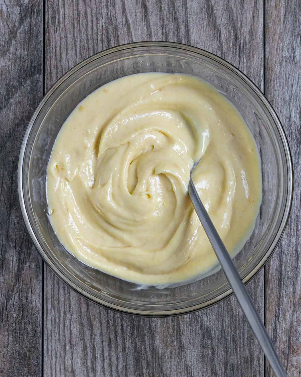 Glass bowl on a wood grained board with miso mayo ingredients mixed with a spoon.