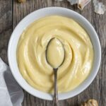 White serving bowl of miso mayo with a fancy spoon of mayo floating in the center of the bowl, on a board with whole ginger pieces.