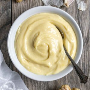 Homemade miso mayonnaise in a white bowl with a serving spoon in the bowl on a wood board.