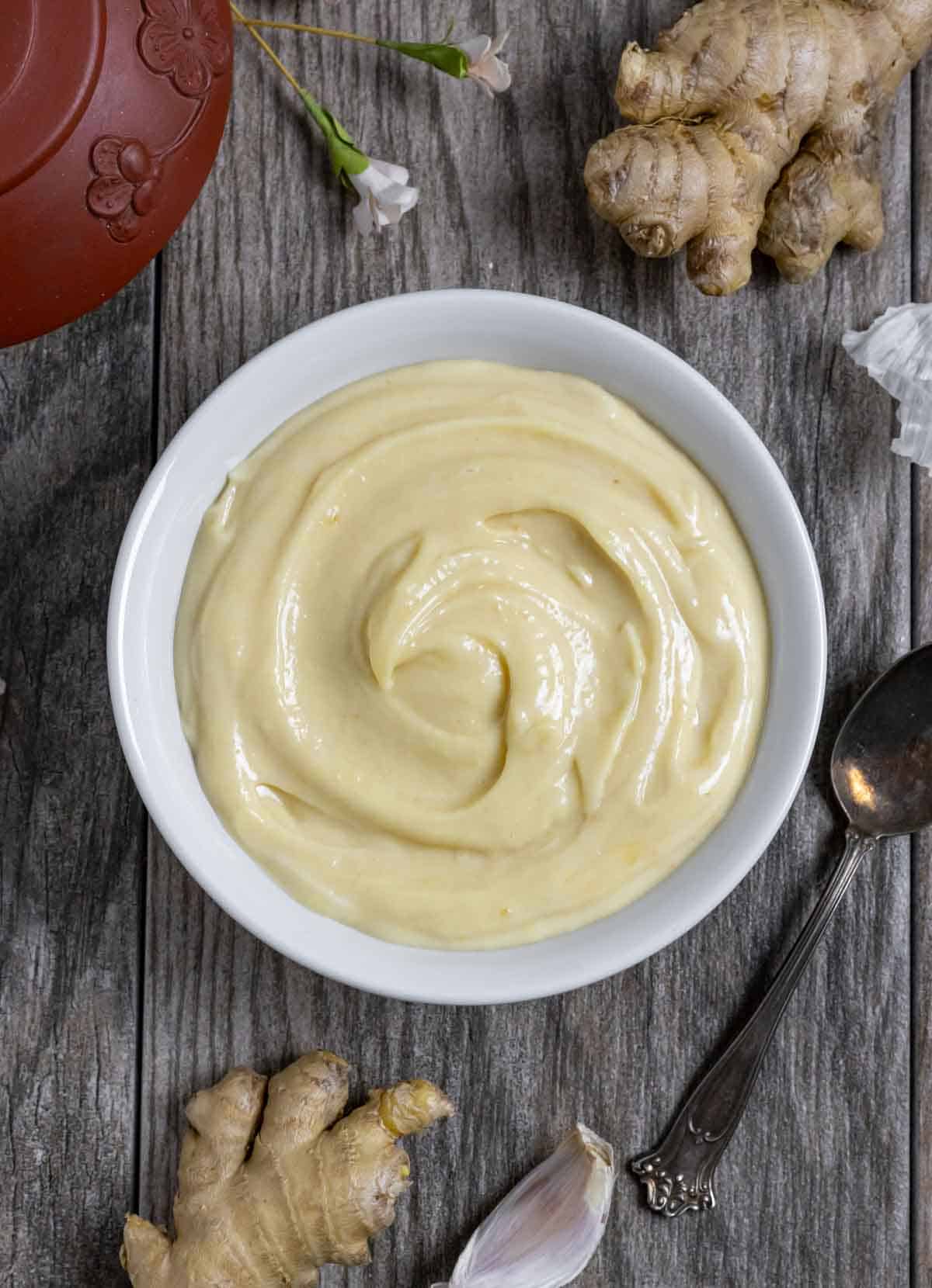 White bowl of creamy miso mayo on a board next to a clay teapot and whole ginger.