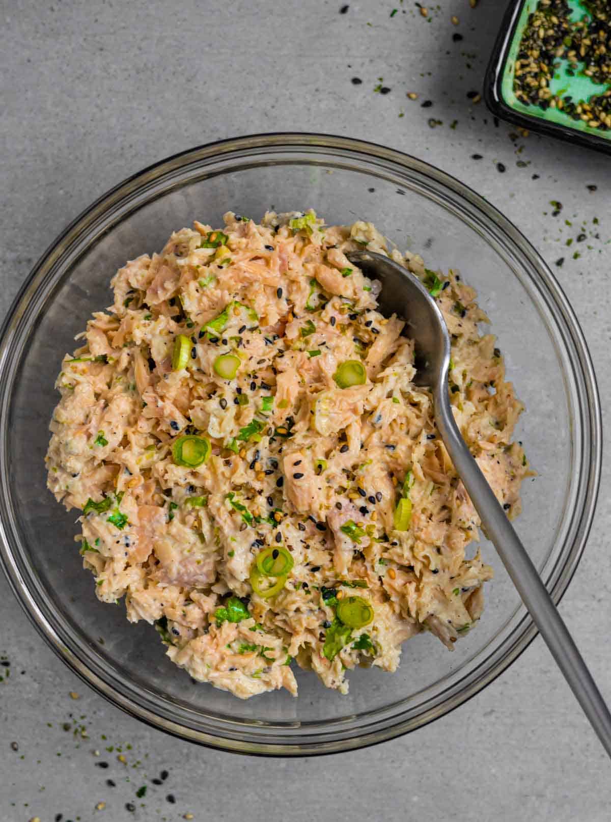 Bowl of miso tuna salad with a serving spoon in it on a grey board with a small bowl of furikake.