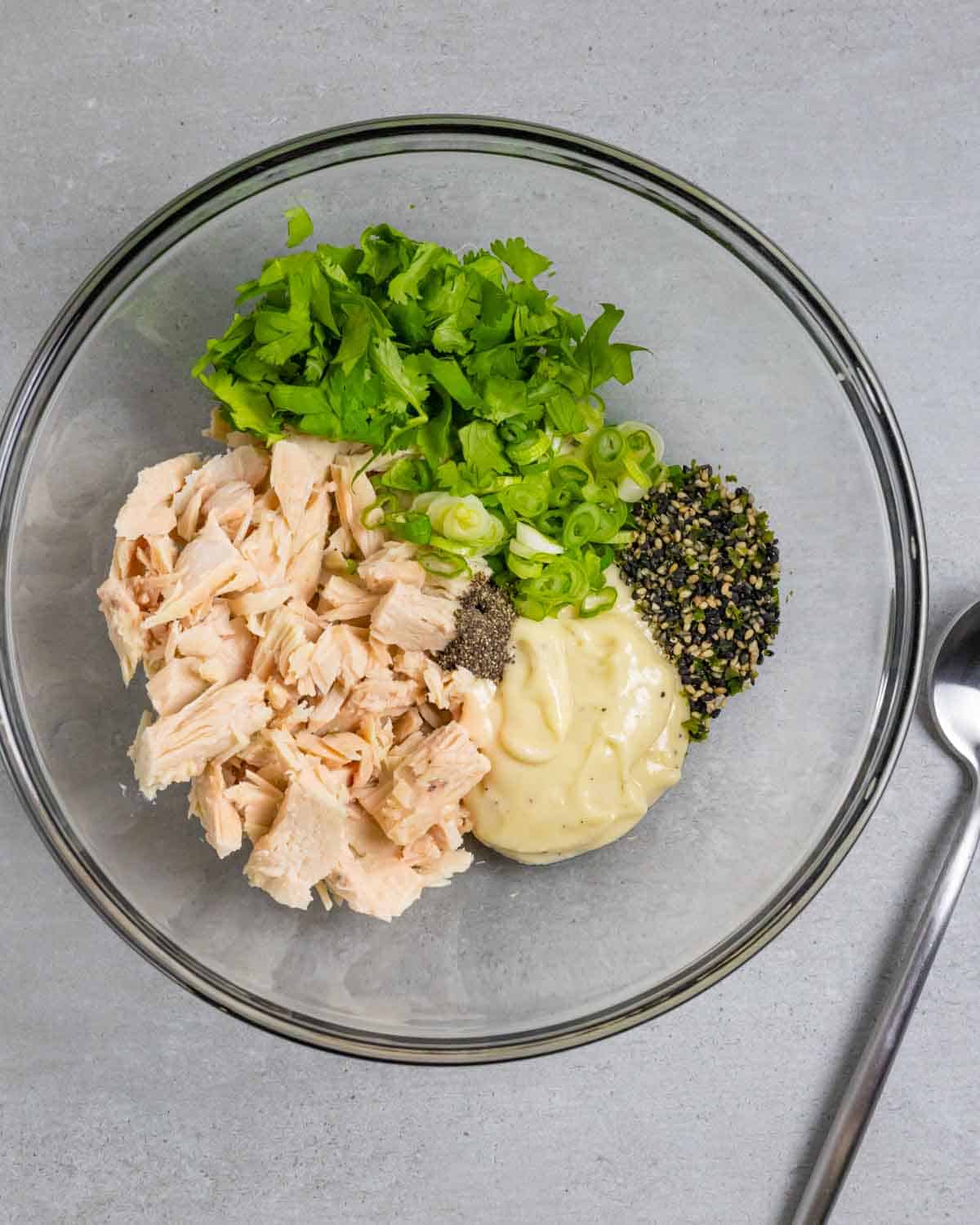 Clear glass bowl containing ingredients for miso mayo in piles, on a grey board with a mixing spoon.