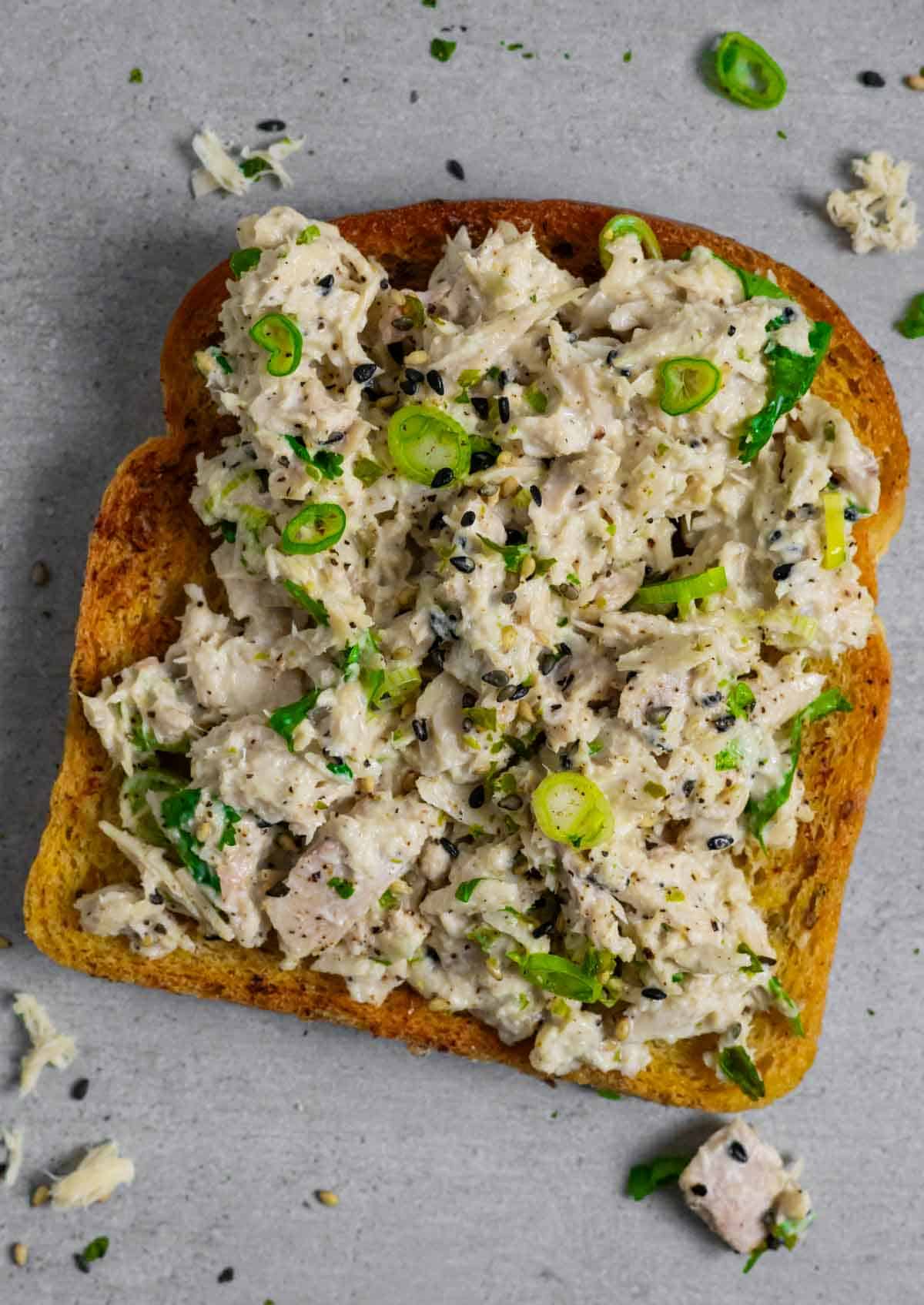 Miso tuna salad on toast on a grey board with tuna and herbs.